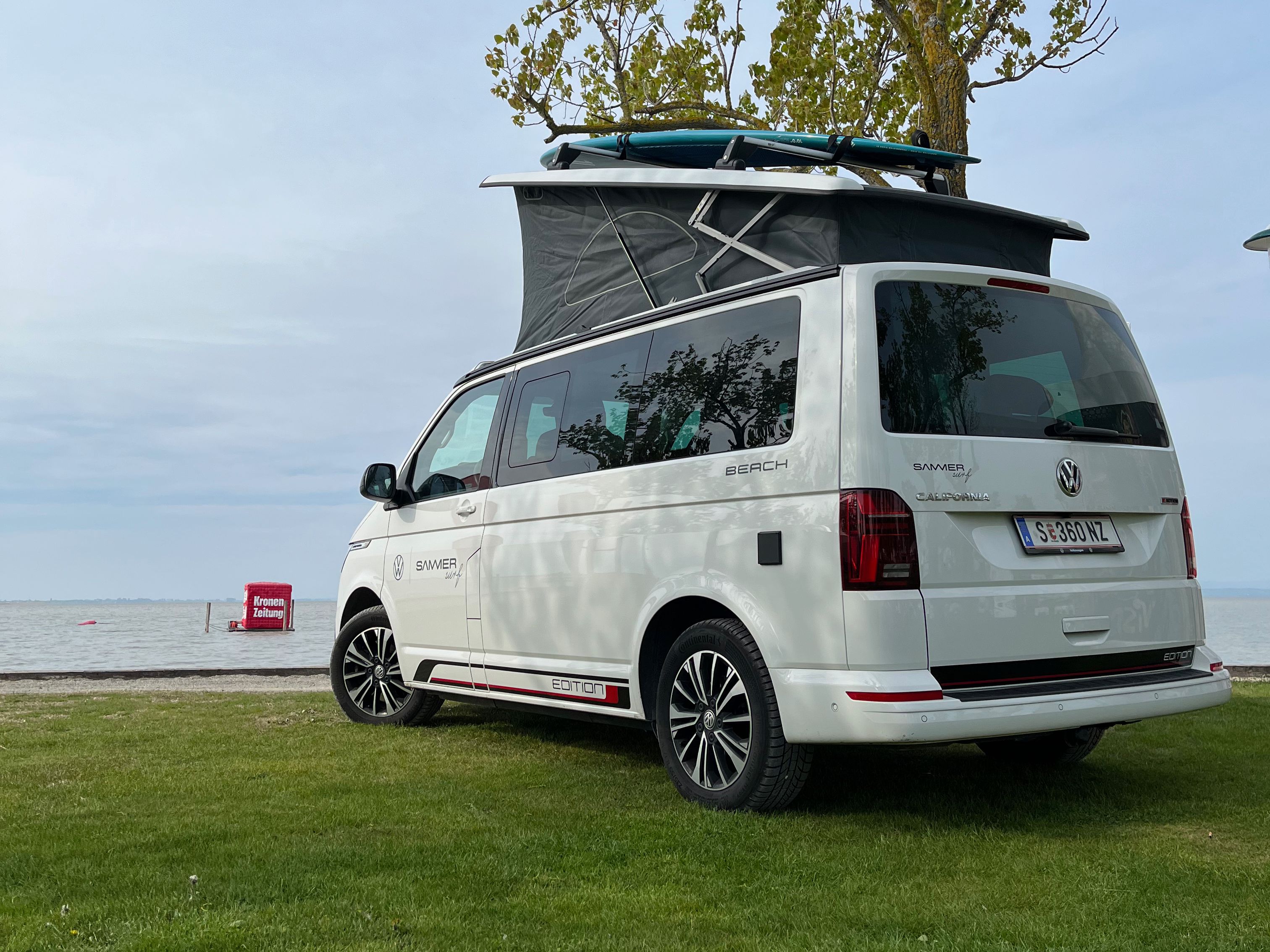 VW California Beach mit ausgeklapptem Dach parkt neben dem Meer