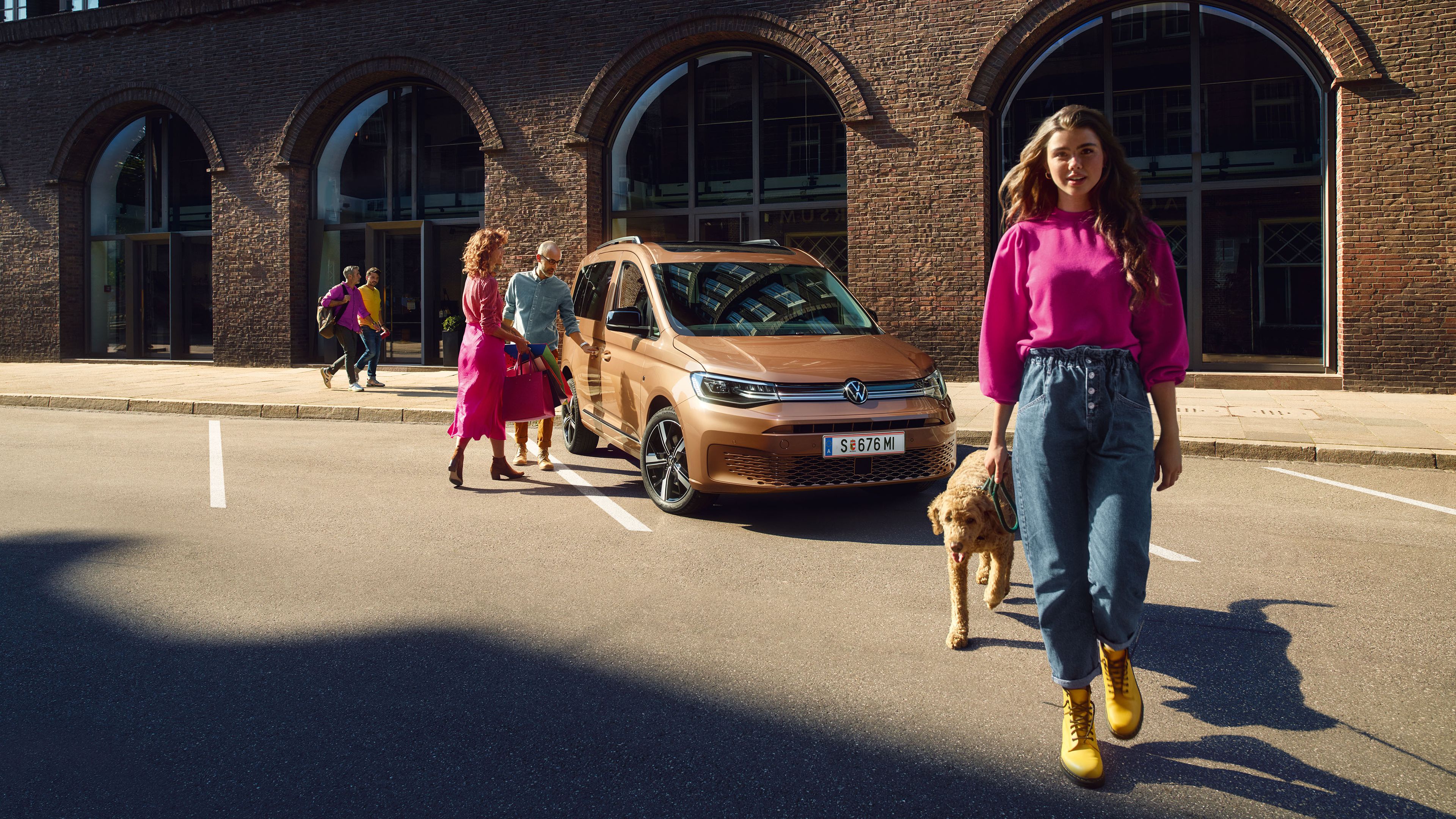 VW Caddy Cargo in Copper Bronze. Familie mit Hund stehen in der Nähe.