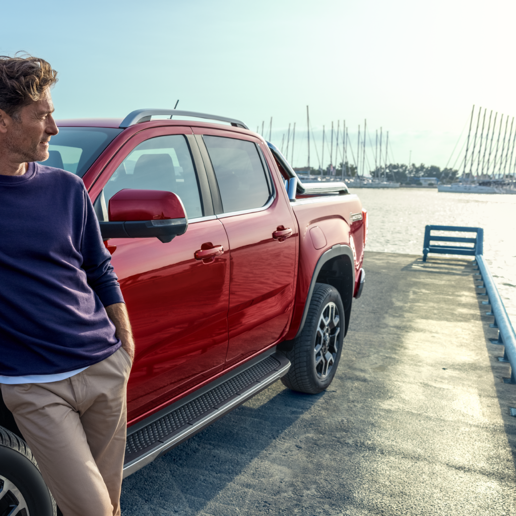 Mann lehnt an neuem Amarok, der am Hafen steht, und blickt über das Wasser