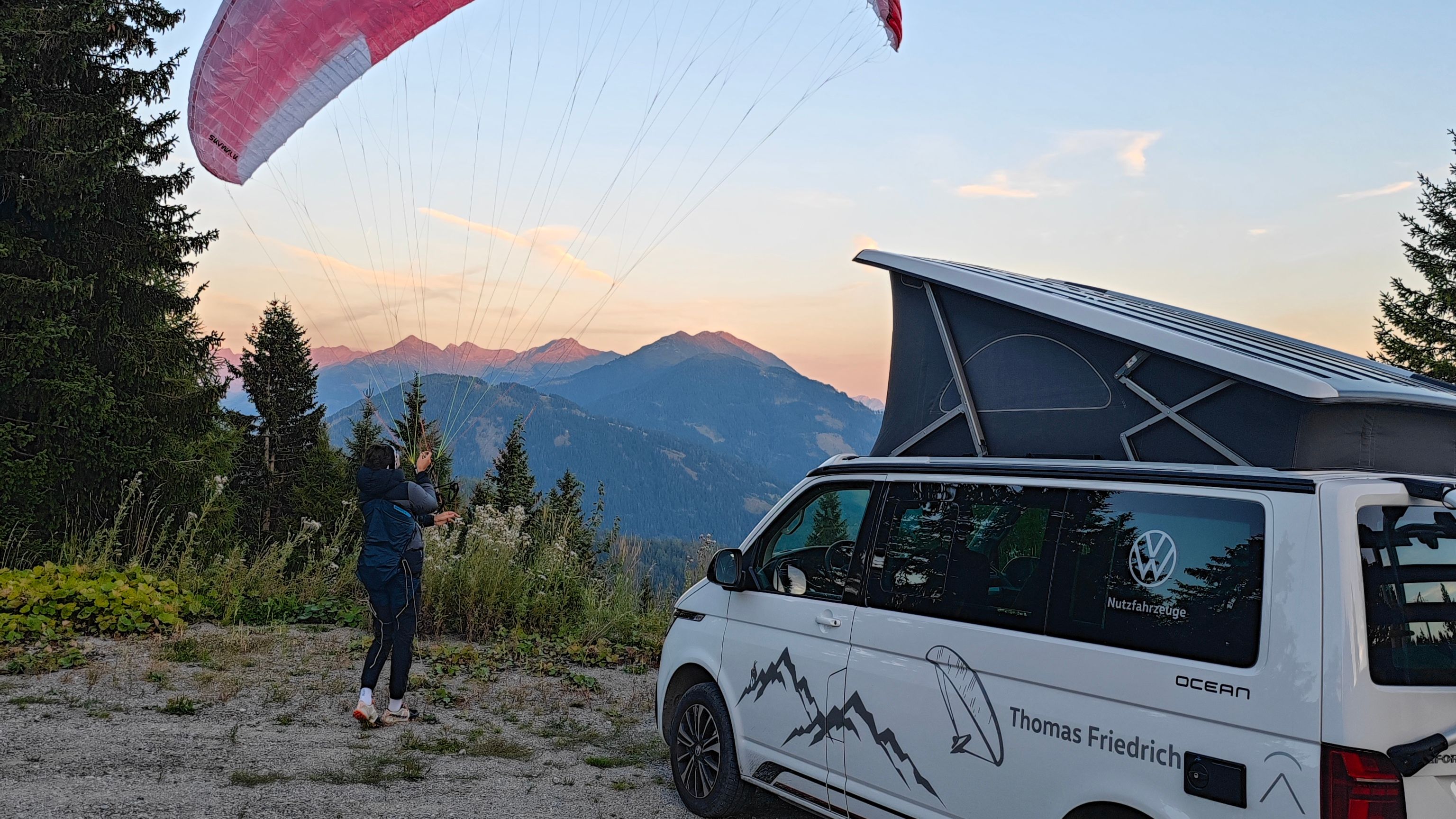 Thomas Friedrich steht mit gespanntem Paragleitschirm neben einem VW California Ocean mit ausgeklapptem Dach