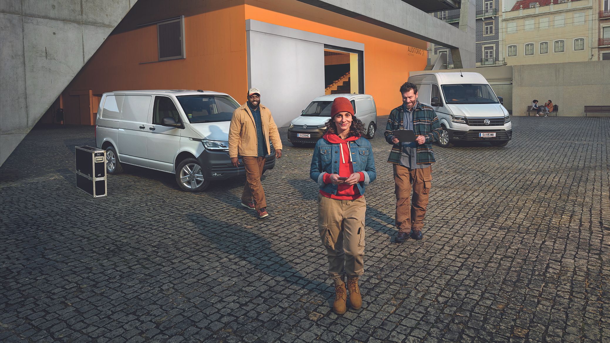 Weißer Crafter Kastenwagen, weißer Caddy Cargo und weißer Transporter Kastenwagen stehen auf einem Parkplatz vor einem Gebäude.