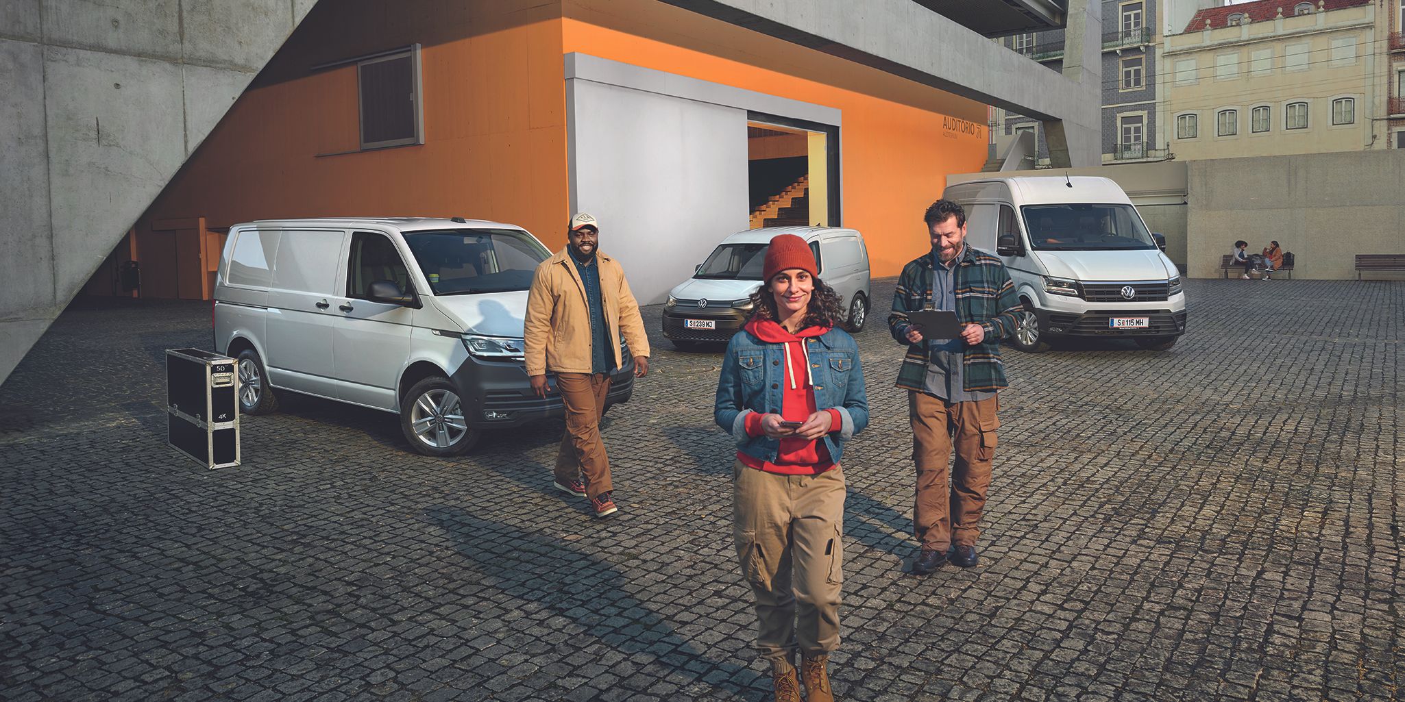 Weißer Crafter Kastenwagen, weißer Caddy Cargo und weißer Transporter Kastenwagen stehen auf einem Parkplatz vor einem Gebäude.