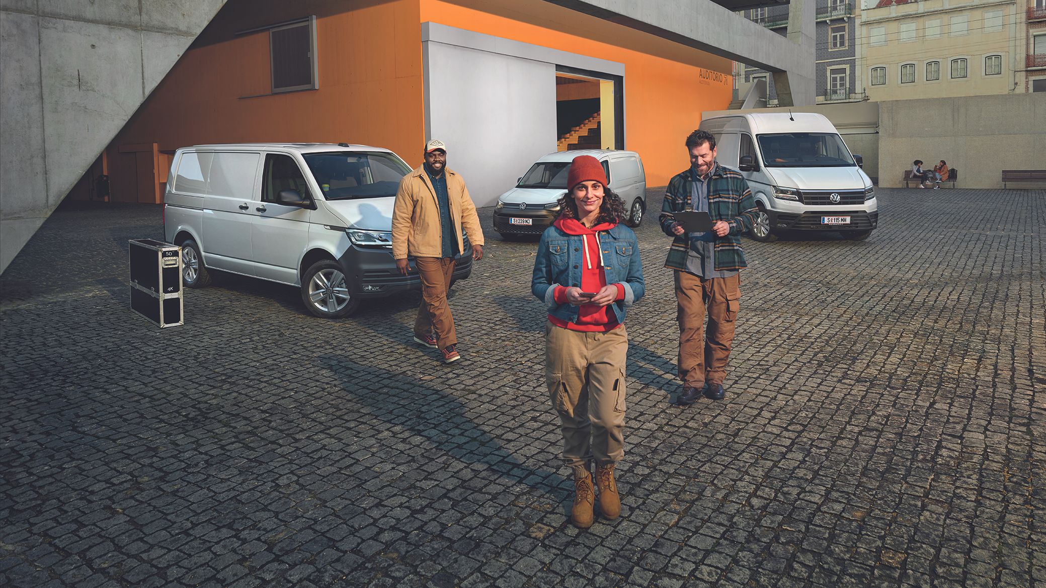 Weißer Crafter Kastenwagen, weißer Caddy Cargo und weißer Transporter Kastenwagen stehen auf einem Parkplatz vor einem Gebäude.