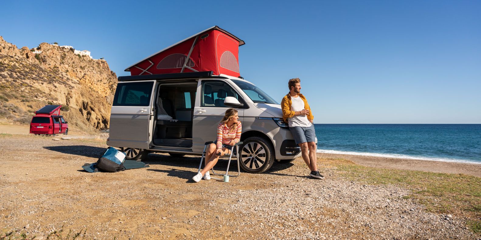 Ein Volkswagen California an einem Strand mit ausgefahrenem Aufstelldach