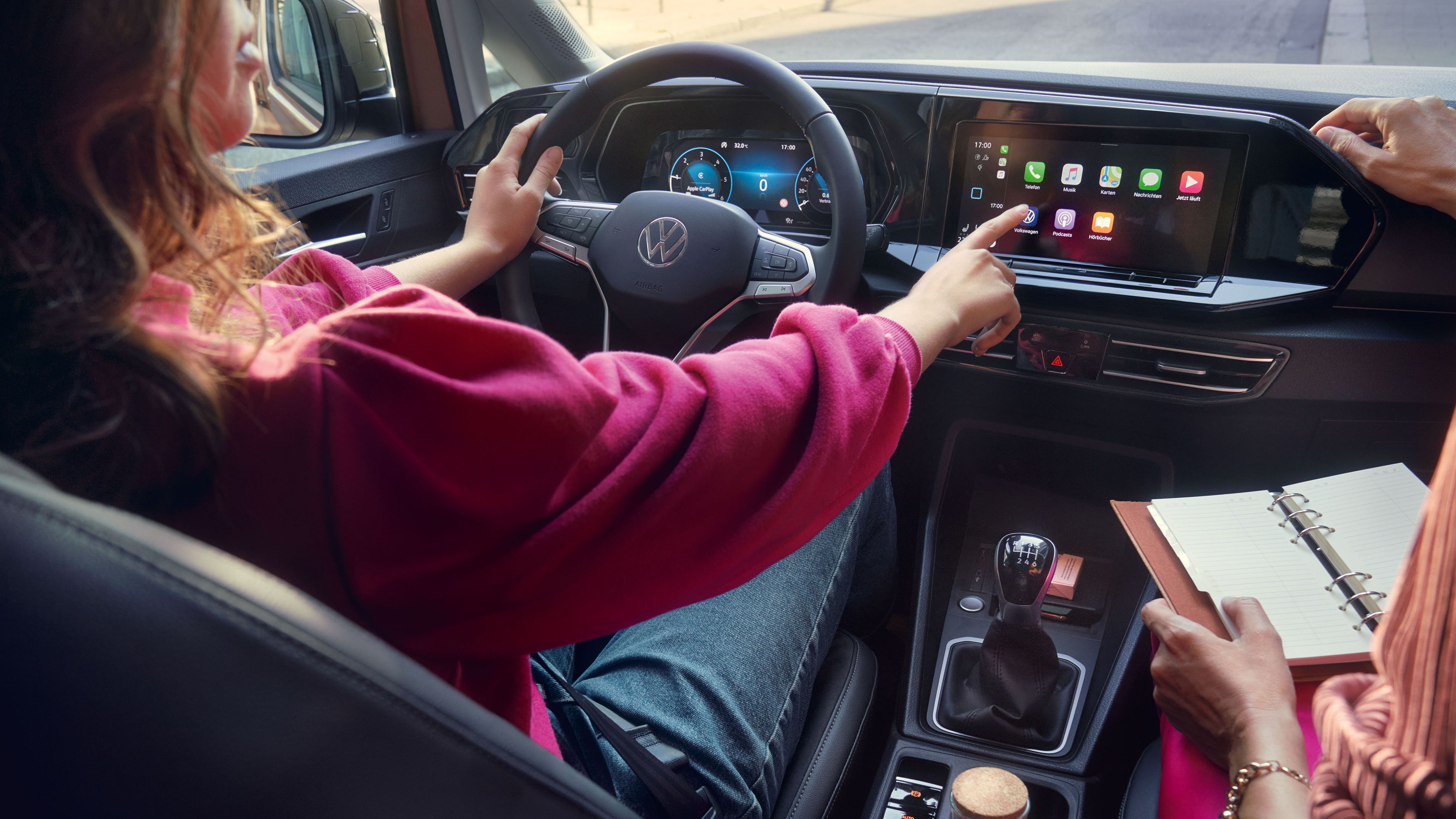 Frau sitzt im VW Caddy California und bedient das Display. 