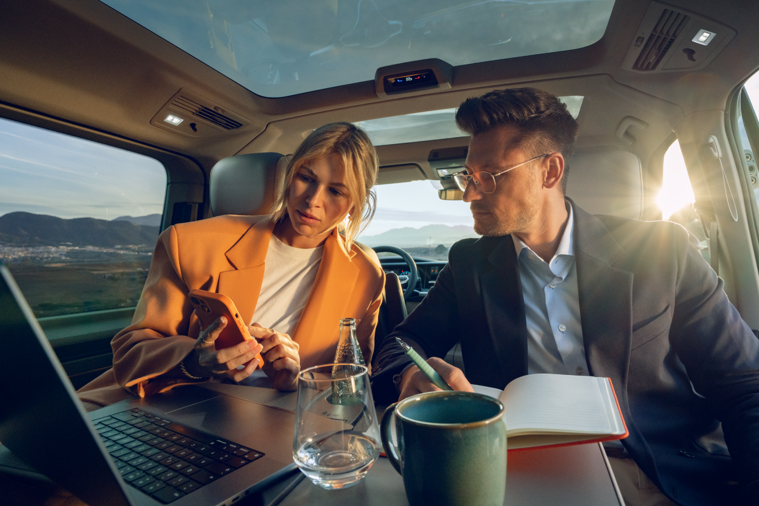 Mann und Frau sitzen im Fond eines neuen VW Multivans, ausgeklappter Tisch, schauen auf Laptop