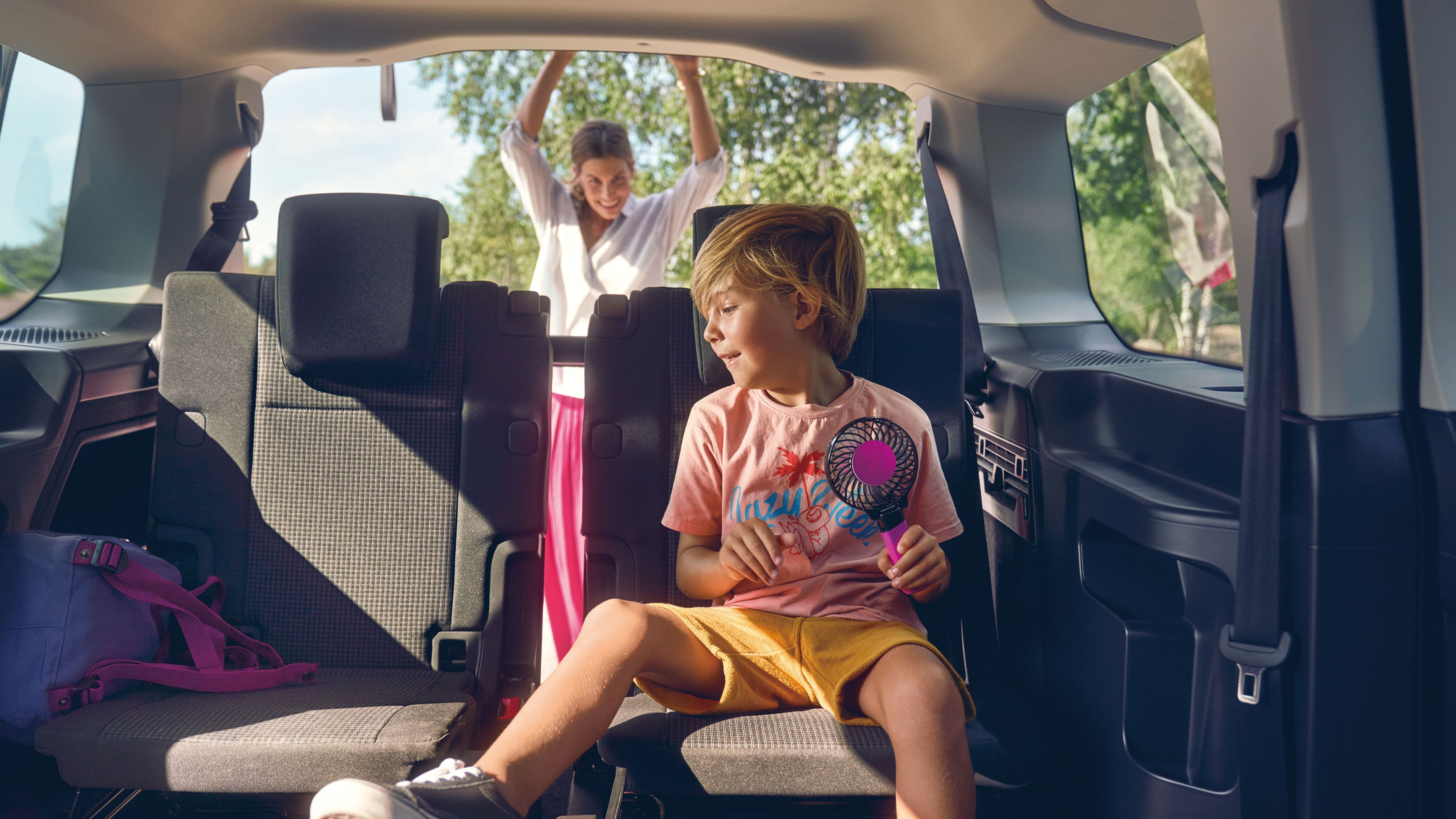 Ein Junge sitzt auf der Rückbank eines VW Caddy 5, seine Mutter schließt die Heckklappe 