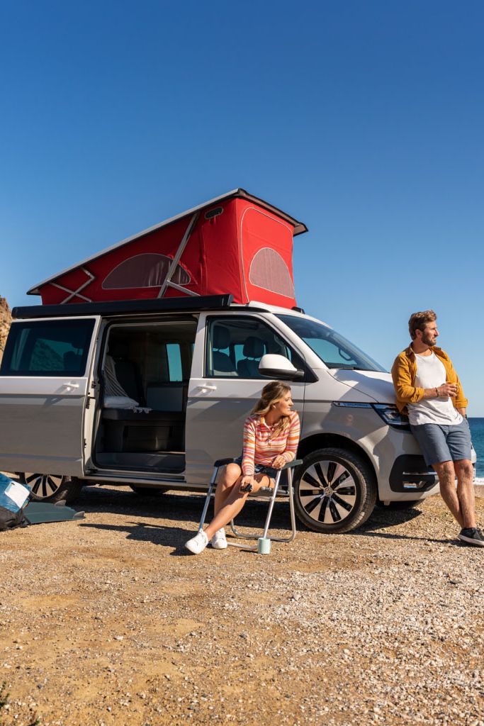 Ein Volkswagen California an einem Strand mit ausgefahrenem Aufstelldach