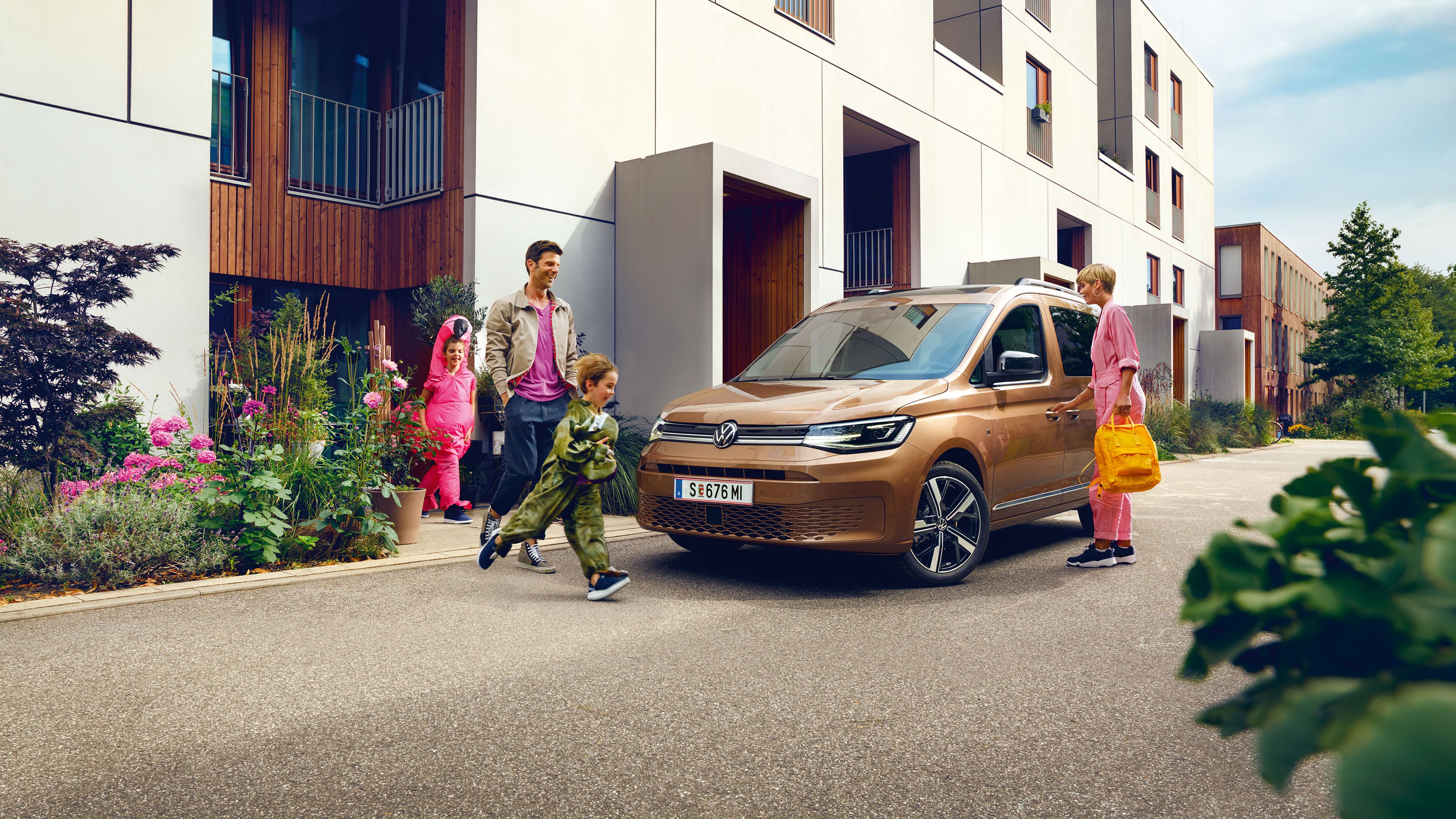 Eine junge Familie steigt vor der Wohnung in einen VW Caddy ein.