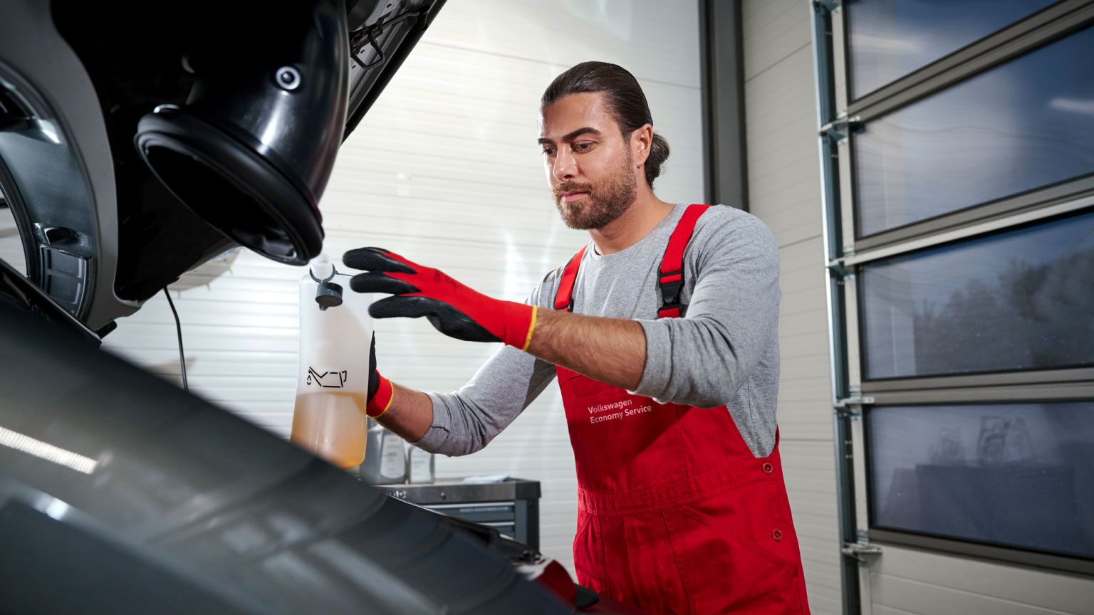 VW Service Techniker beim Nachfüllen von Betriebsflüssigkeit