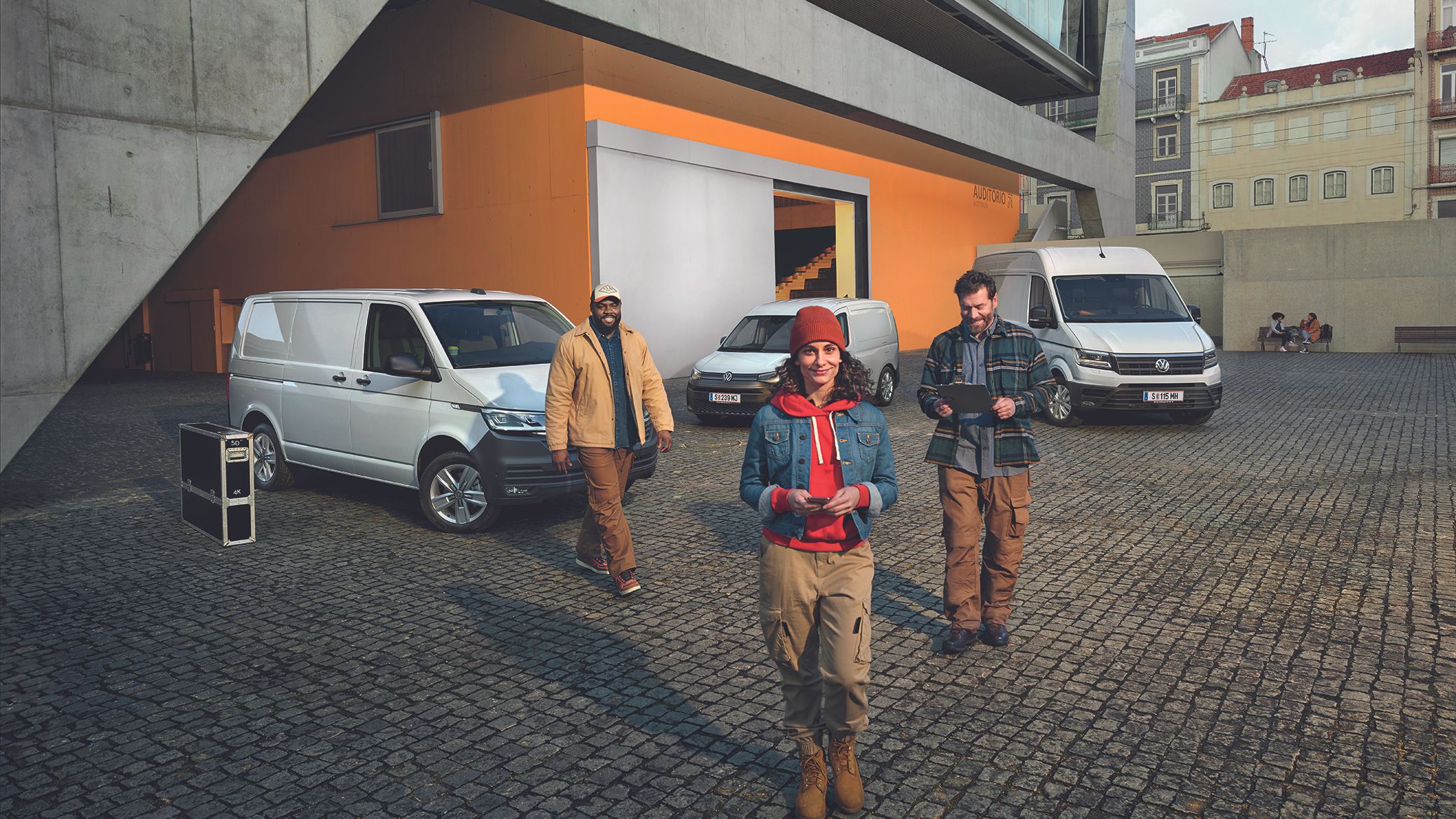 Weißer Crafter Kastenwagen, weißer Caddy Cargo und weißer Transporter Kastenwagen stehen auf einem Parkplatz vor einem Gebäude.