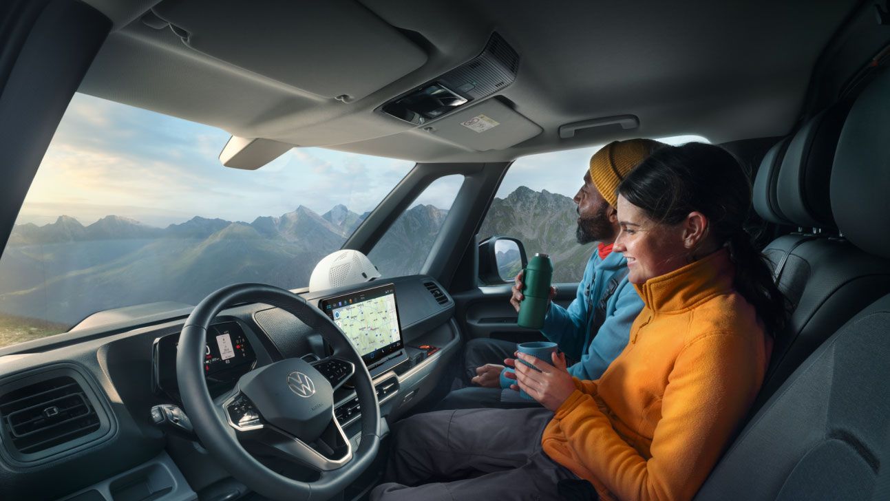 Ein Mann und eine Frau sitzen in einem VW-Nutzfahrzeug und betrachten die Berglandschaft