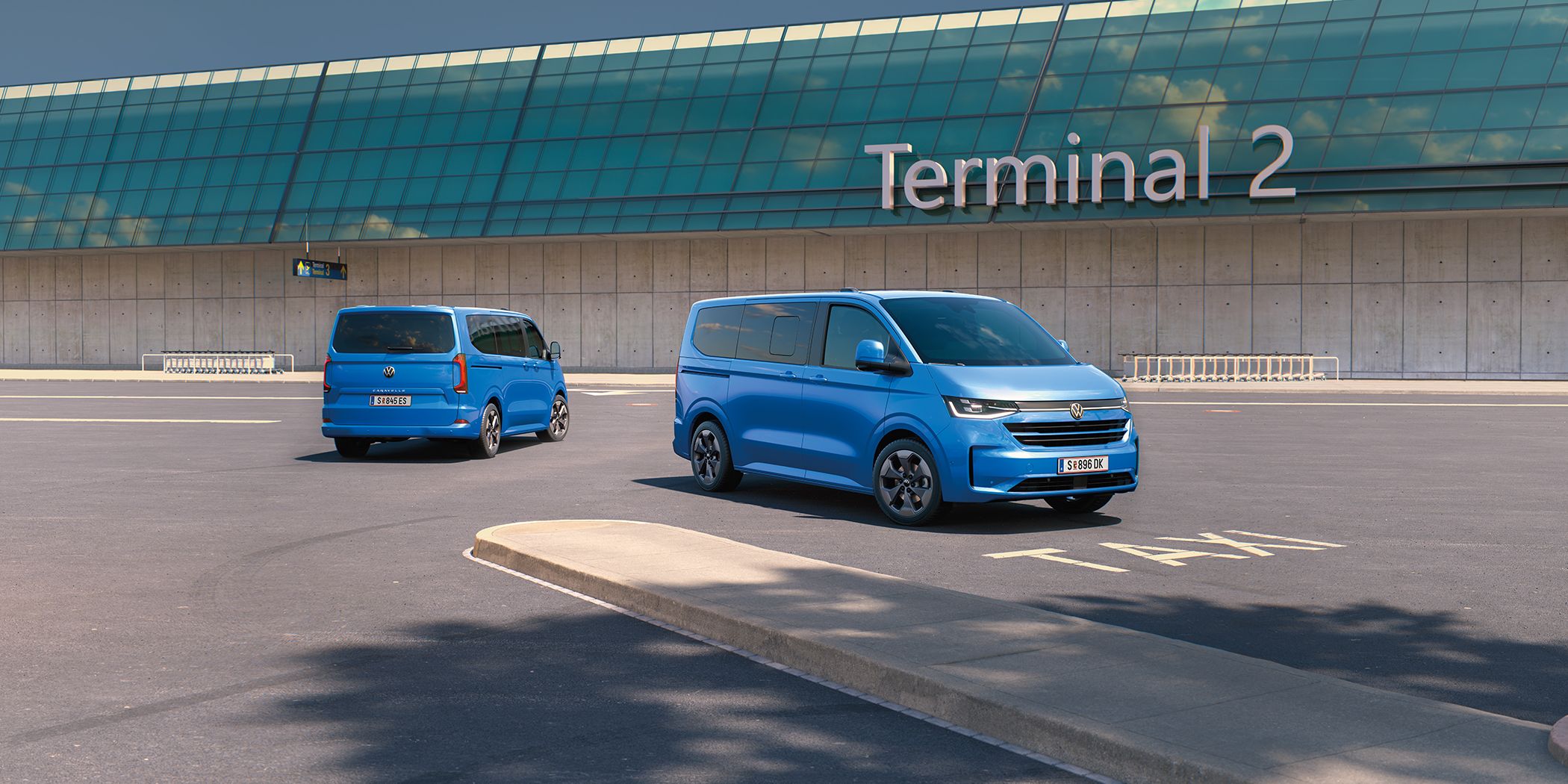 Zwei VW Caravelle stehen vor dem Terminal 2 auf einem Flughafenparkplatz