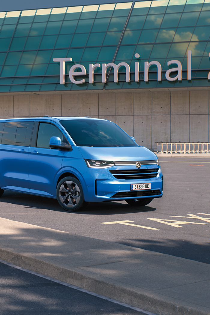 Zwei VW Caravelle stehen vor dem Terminal 2 auf einem Flughafenparkplatz