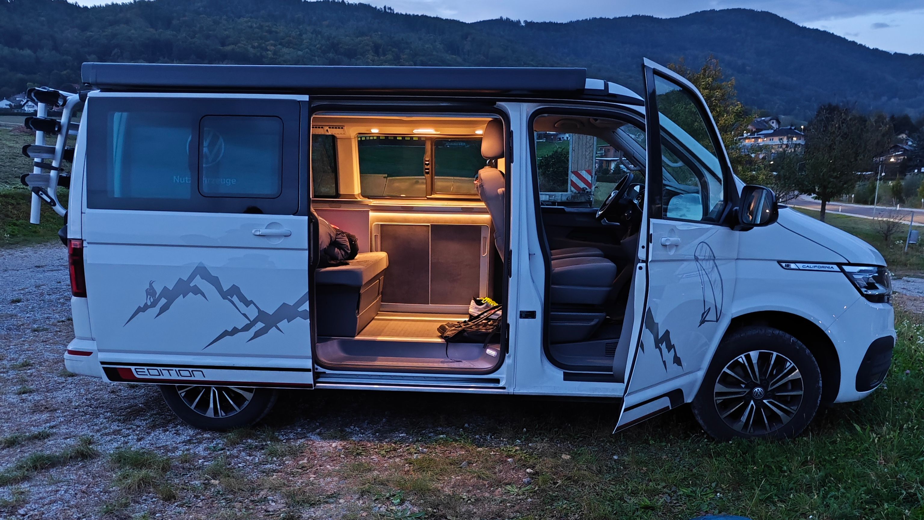 VW California Beach mit geöffneter Schiebe- und Beifahrertüre, Paragleitschirm liegt davor