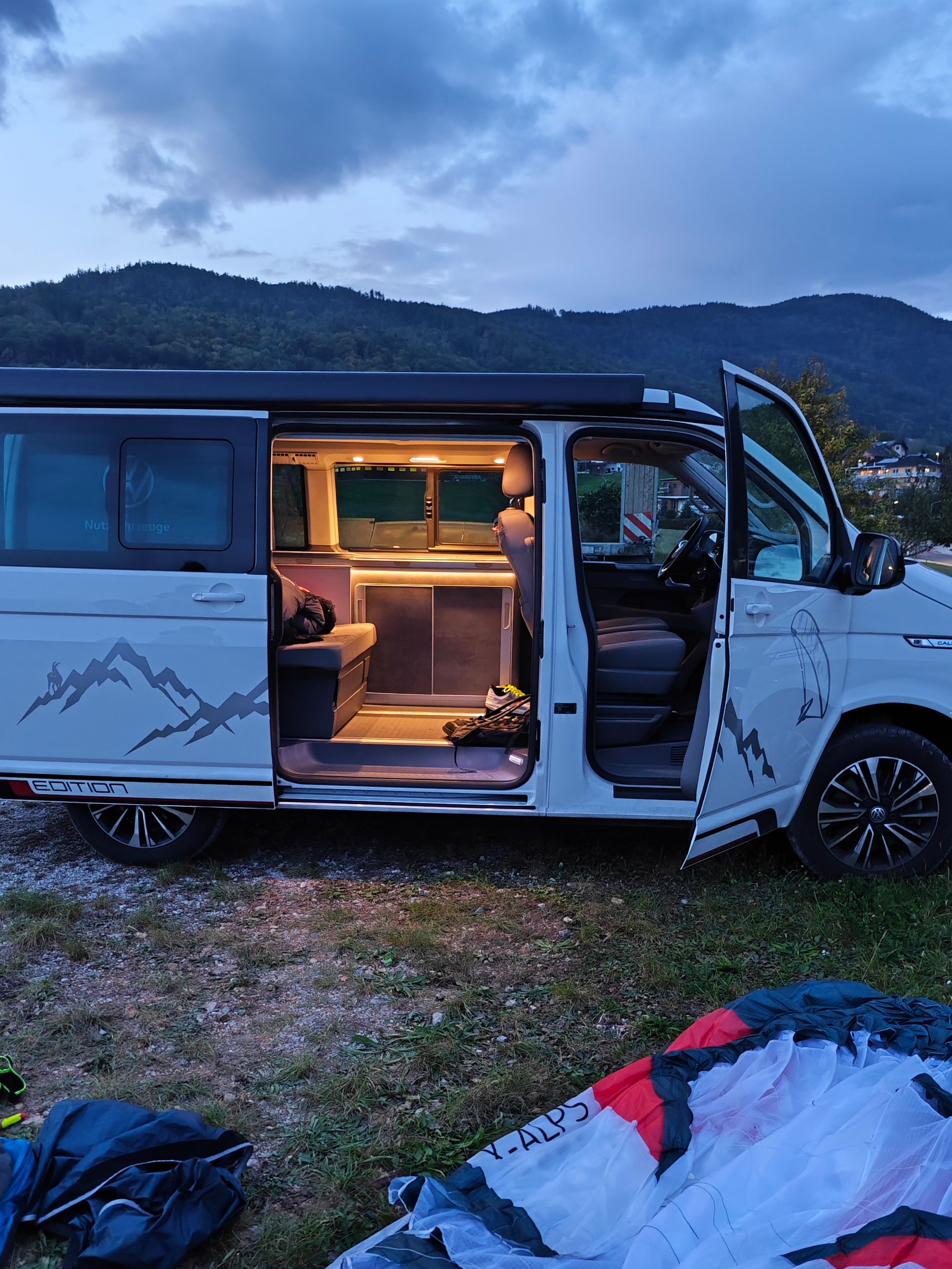 VW California Beach mit geöffneter Schiebe- und Beifahrertüre, Paragleitschirm liegt davor