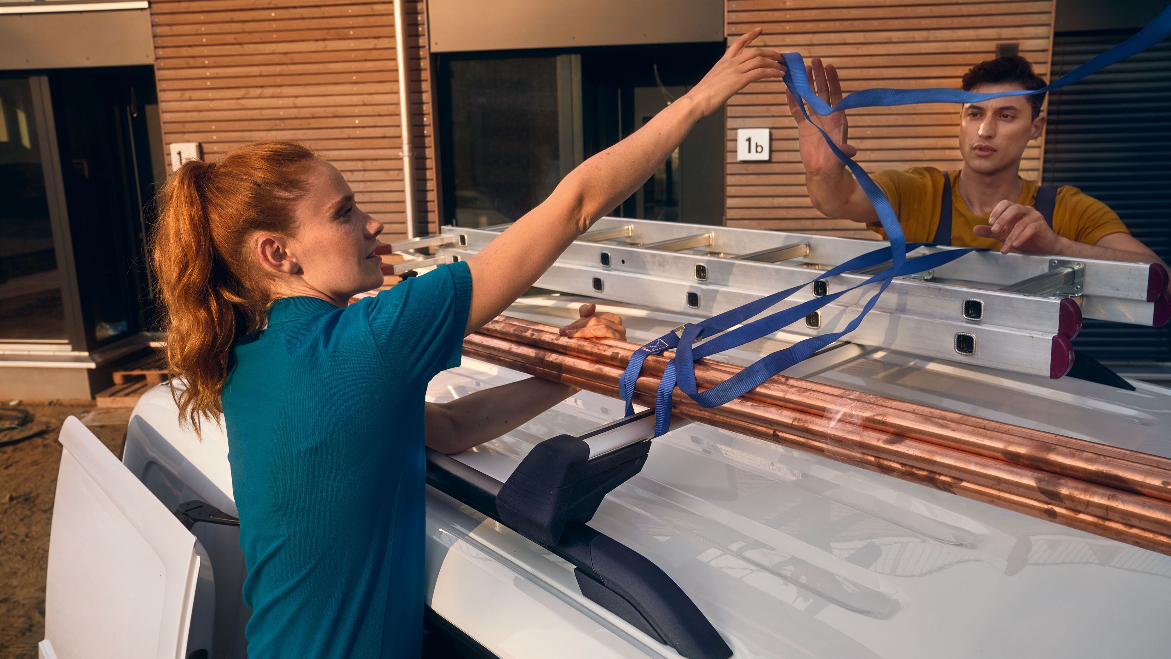 Ein Handwerker-Team fixiert eine Leiter auf der Dachreling eines VW Caddy Cargo.