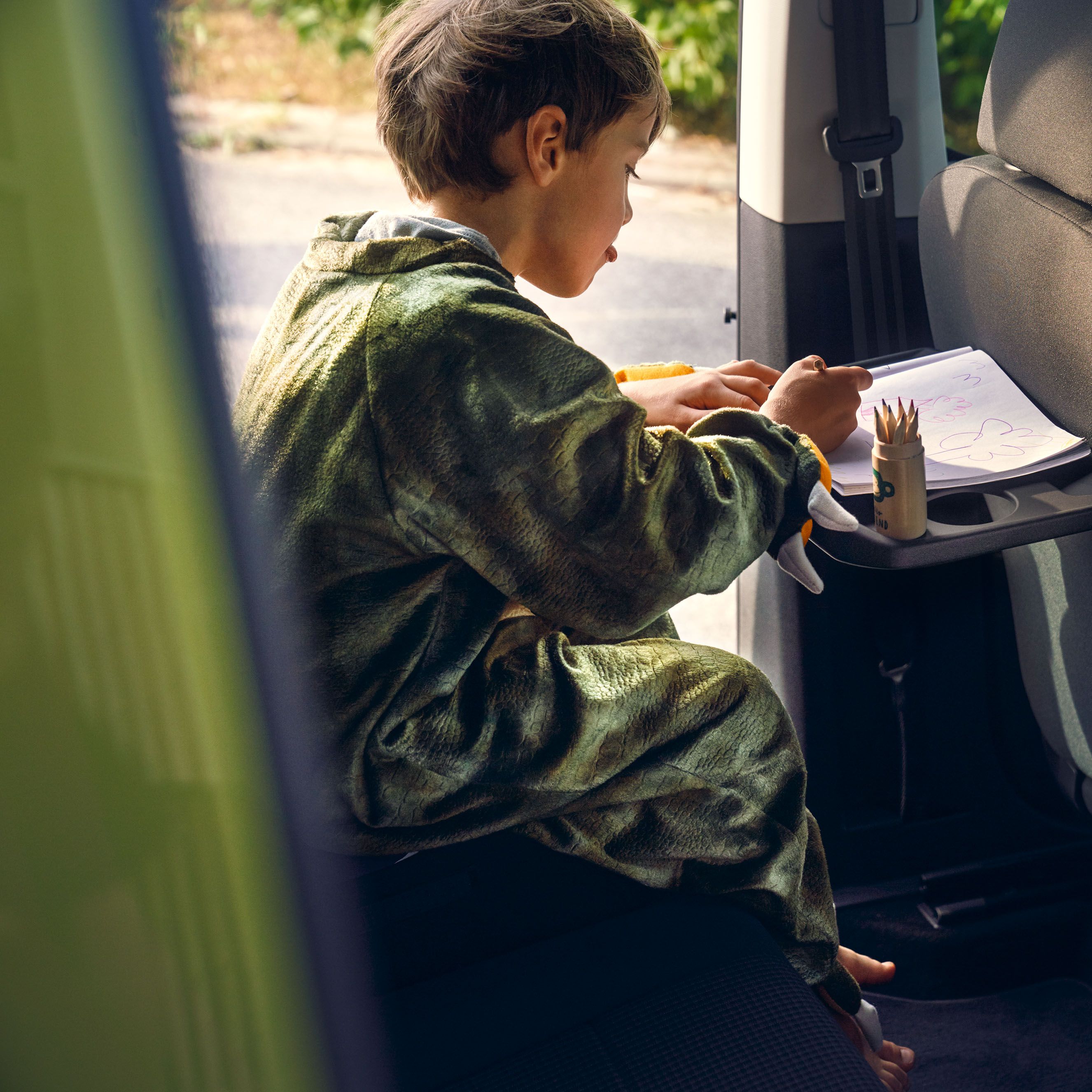 Ein Junge sitzt auf der Rückbank eines VW Caddy 5 und malt