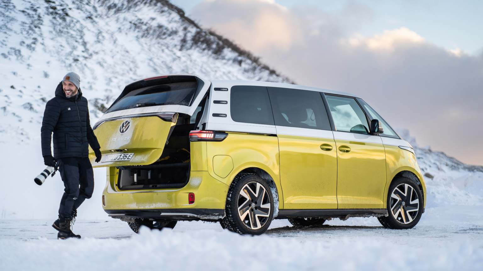 Ein Volkswagen ID. Buzz parkt in winterlicher Landschaft, ein Mann öffnet die Heckklappe.