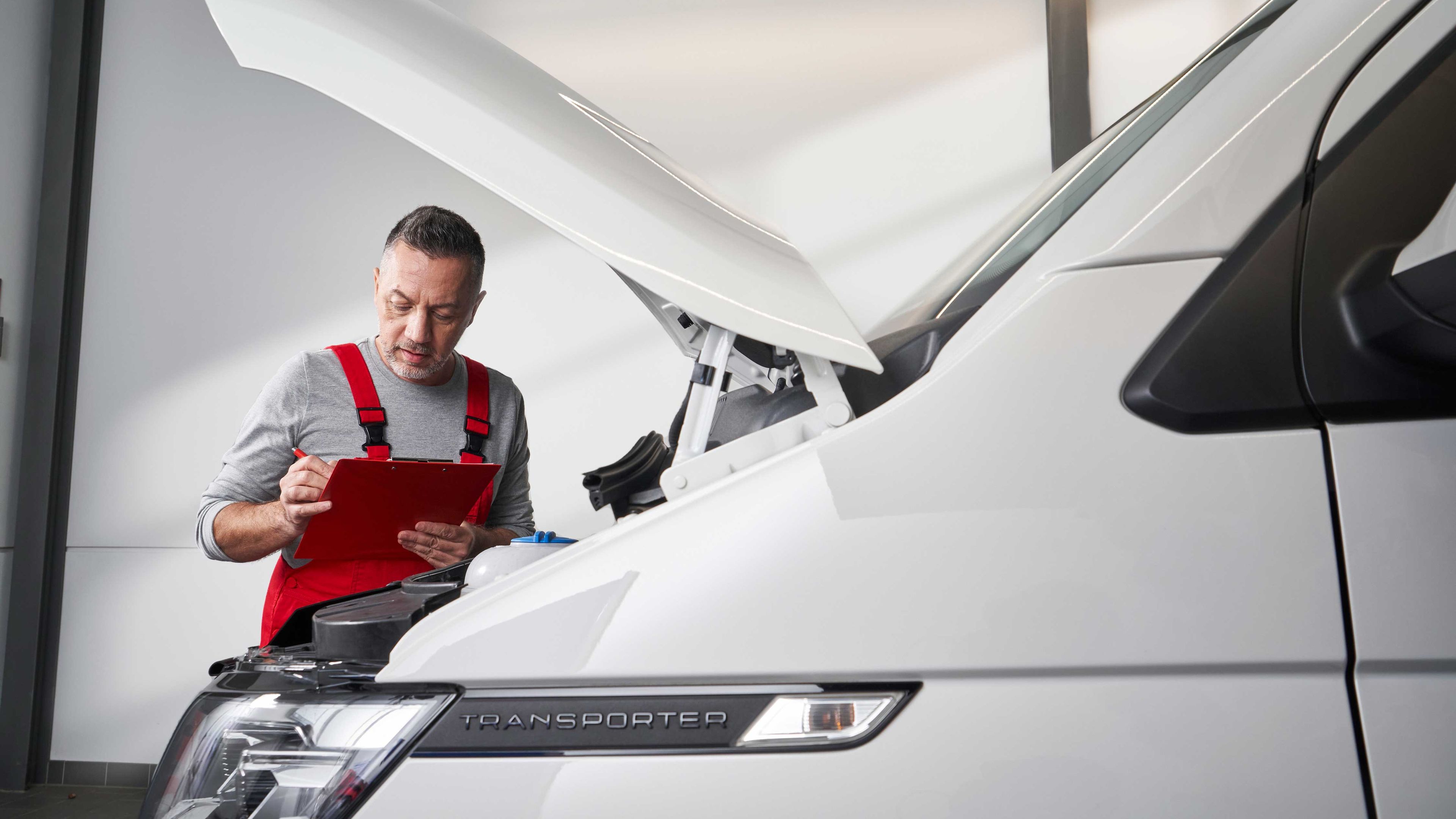 Ein Volkswagen Service Techniker vor einem Volkswagen Nutzfahrzeug mit geöffneter Kühlerhaube