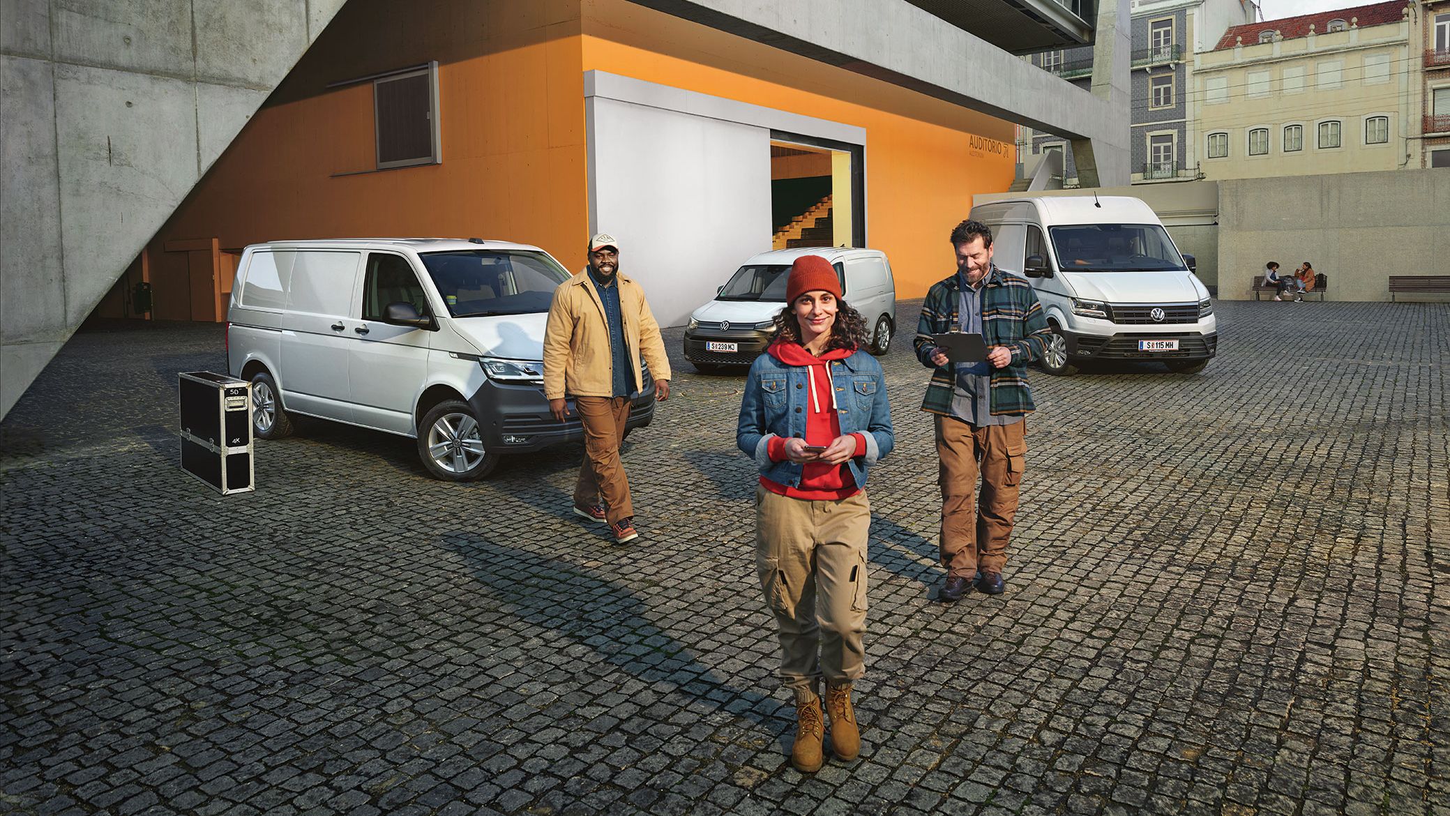 3 weiße VW Nutzfahrzeugmodelle parken. Davor stehen 3 Personen.